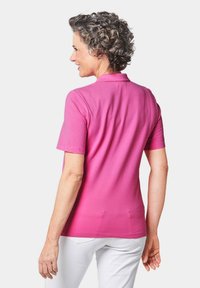 Rosa Polohemd mit kurzen Ärmeln und Kragen, aus weichem Material. Der Rücken hat eine glatte Textur und ein leicht tailliertes Design.