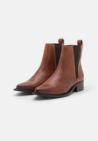 Hnědé kožené kotníkové boty s elastickými postranními panely, špičatou špičkou a malým blokovým podpatkem. Mají hladký povrch a poutka pro snadné obouvání.