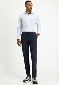 Lichtblauw shirt met lange mouwen en een gestructureerd patroon, gecombineerd met marineblauwe broek met een elastische tailleband, en grijze sneakers met zwarte accenten.