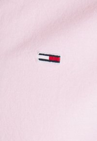 Hellrosa Stoff mit einem gestickten Logo, das ein rechteckiges Design in den Farben Rot, Weiß und Schwarz zeigt.