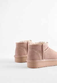 Rosa mockaläder stövletter med en mjuk, beige pälsfoder och en låg gummisula. Har dekorativ sömnad och en rundad tåsdesign.