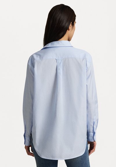 Chemise bleu clair à manches longues avec une coupe décontractée, poignets boutonnés, détail de plis au dos et ourlet arrondi. Texture en coton lisse.