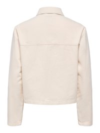 Bēša ikdienas jaka ar garām piedurknēm, taisnu apakšu un vienkāršu aizmuguri ar yoke šuvi pāri pleciem.