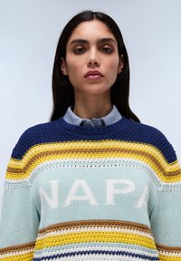 Gebreide trui met horizontale strepen in blauw, geel, beige en wit op een lichtblauwe basis; "NAPA" tekst in crème over de borst.