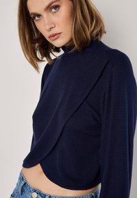 Marineblaues, gestreiftes Langarmoberteil mit einem hohen Kragen und drapiertem Vorderteil, kombiniert mit hellblauen, hoch taillierten Jeans. Weicher Stoff.
