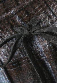 Brunt och blå mönstrad tyg med en mjuk textur, som har en mörk vävd dragsko knuten i en rosett i mitten.
