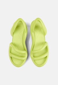 Vihreät sandaalit, joissa on sileä, kumimainen pinta, leveät ristikkäisnarut ja pehmustettu pohja, jossa on muotoiltu malli.