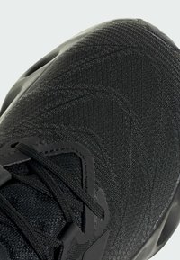 Black athletic shoe featuring a textured fabric upper with a mesh pattern, reinforced eyelets for laces, and a solid rubber sole for grip.