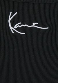 Juodas juostuotas audinys su baltu kursyvu išsiuvinėtu vardu "Kani". Tekstūra yra minkšta, o dizainas pabrėžia prigludusį siluetą.