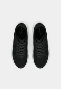 Μαύρα αθλητικά παπούτσια με δίχτυ, λευκές σόλες και μαύρα κορδόνια με λευκές κουκκίδες, απεικονιζόμενα από πάνω σε λευκό φόντο.