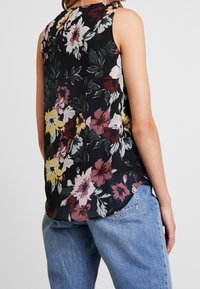 Floral sleeveless top with a black background, featuring large flowers in red, yellow, and white. Lightweight, semi-sheer fabric, rounded hem.