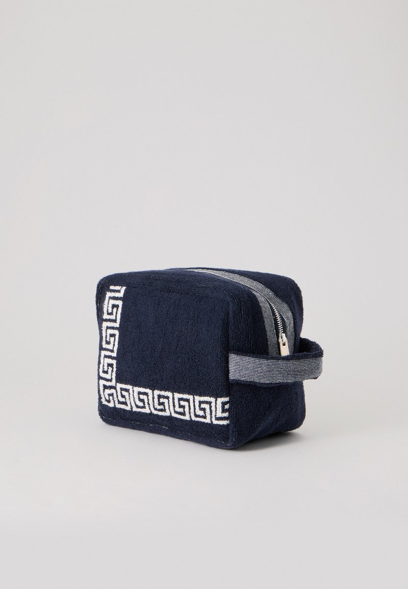 Trousse de toilette rectangulaire bleu marine avec motif clé grecque blanc, fermeture éclair grise et poignée latérale sur un fond uni clair.
