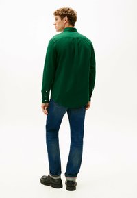 Groene overhemd met lange mouwen en knopenmanchetten, achterste plooi, gecombineerd met blauwe jeans en zwarte schoenen. Glad textuur, tailored fit.