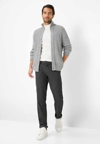 Grijze gebreide cardigan met kabelpatroon, knoopsluiting en ribbels om de mouwen, gecombineerd met donkergrijze broeken en witte sneakers.