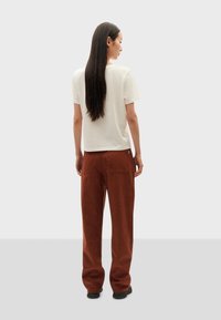White short-sleeve t-shirt paired with loose-fit, rust-colored trousers featuring two back pockets and minimalistic design.