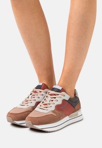 Zapatillas de mujer con diseño de múltiples materiales en marrón, burdeos y gris. Cuenta con una parte superior texturizada, cordones y acentos de marca.