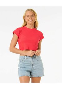 T-shirt rossa a maniche corte, cropped, con texture a coste e scollo rotondo, abbinata a pantaloni shorts di jeans blu chiaro con tasche frontali.