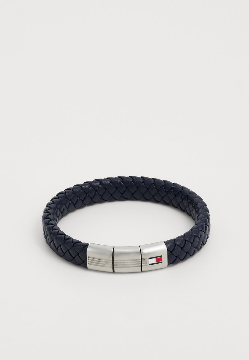 Tumedast sinine punutud nahast käevõru, millel on hõbedane magnetklamber, millel on väike ristkülikukujuline punase, valge ja sinise logoga.