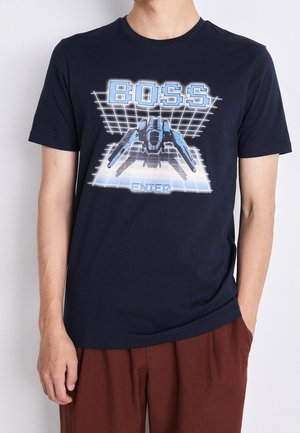 T-shirt en coton bleu marine avec un design graphique d'un vaisseau spatial et le mot "BOSS" en bleu clair, sur fond de motif en grille.