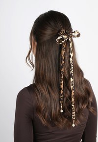 Haarband im Leopardenmuster mit langen Bändern und Perlenakzenten, aus weichem Stoff, befestigt an frisiertem braunem Haar.
