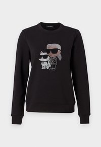 Sweat-shirt noir à manches longues avec un motif en strass représentant une personne aux cheveux blancs et lunettes de soleil, debout à côté d'un chat portant également des lunettes de soleil.