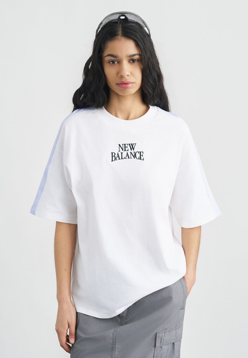 Λευκό υπερμεγέθες t-shirt με κεντημένο λογότυπο "NEW BALANCE" σε μαύρο χρώμα. Κοντά μανίκια με μπλε λεπτομέρειες, κατασκευασμένο από μαλακό βαμβακερό ύφασμα.