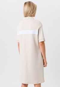 Robe beige à manches courtes et col montant. Dotée d'un panneau en maille blanche au dos. Texture lisse, design à hauteur des genoux.