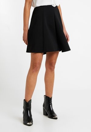 Woman wearing a black A-line skirt with textured fabric, paired with shiny black ankle boots featuring silver toe caps and side zippers.