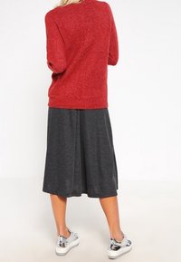 Maglione rosso realizzato in morbido tessuto a maglia, abbinato a una gonna plissettata grigia. Presenta sneakers argento con una superficie liscia e lucida.