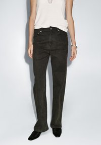 Dunkelblaue Jeans aus Denim mit geradem Bein, fünf Taschenstil und vorderem Knopfverschluss. Kombiniert mit einem weißen Tanktop und schwarzen Schuhen.