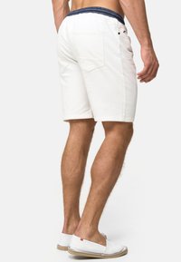 Witte katoenen shorts met een marineblauwe elastische tailleband, twee achterzakken en een slim fit, gecombineerd met witte instappers met een beige zool.