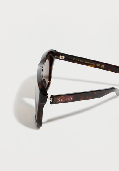 Γυαλιά ηλίου ταρταρούγα με σκούρους φακούς, που δείχνουν το λογότυπο "GUCCI" στον κροτάφο και την εγχάραξη "Made in Italy" στην εσωτερική πλευρά του βραχίονα.