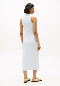Jasnoniebieska sukienka bez rękawów z kołnierzykiem, dopasowana, o długości do połowy łydki, gładka w dotyku, zestawiona z płaskimi sandałami i minimalistyczną biżuterią.