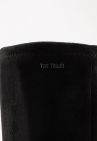 Stivale in suede nero con texture liscia, caratterizzato da un bordo superiore dritto e un sottile dettaglio cucito. Piccolo logo "TOM TAILOR" impresso.
