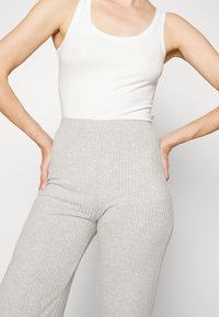 Grå ribbade vida byxor med hög midja, tillverkade av en mjuk jersey, i kombination med en åtsittande vit tank top.