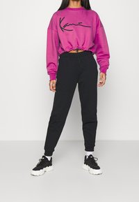 Sudadera corta morada con un logo negro, combinada con pantalones jogger negros y zapatillas negras con suelas blancas.