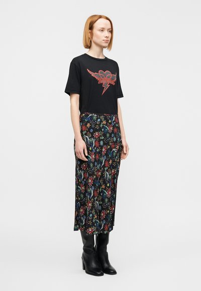 Μαύρο γραφικό t-shirt με κόκκινες διακοσμήσ εις και σχέδιο αστραπής, συνδυασμένο με μαύρη φούστα με λουλουδάτο μοτίβο; το μοντέλο φοράει μαύρες μπότες μέχρι το γόνατο.