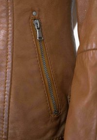 Brown leather jacket detail with a silver zipper, textured finish, prominent stitching, and a snap button near the zipper area.