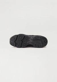 Semelle noire de sneaker New Balance avec motifs sur la bande de roulement et logo, vue du dessous sur un fond clair uni.