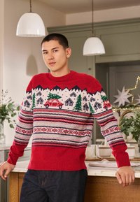 Red knitted sweater featuring winter-themed patterns, including mountains, houses, trees, and a car. Ribbed cuffs and hem, textured fabric.