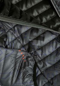 Indvendig sort quiltet jakke med en glat tekstur, lynlåslukning og trykte geometriske mønstre i blå og orange på en mørk baggrund.