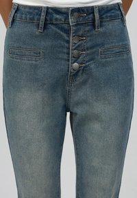 High-waisted denim jeans in light blue with a button-fly closure, two front pockets, and a slightly faded texture.