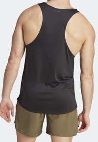 Débardeur noir sans manches à texture lisse et emmanchures larges, associé à un short vert olive, présentant une coupe décontractée.