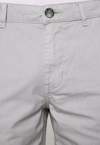 Lichtgrijze katoenen shorts met een knoopsluiting, voorzakken en gestikte details langs de naden. Gladde textuur.