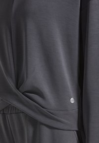 Donkergrijze stof met een gladde textuur, voorzien van een gedraaide ontwerp bij de taille en een klein logoaccent in een zilverkleurige tint.