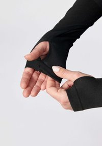 Svart långärmad skjorta med tumhål, tillverkad av ett slätt, stretchigt tyg och en kroppsnära design, där händer justerar manschetten.