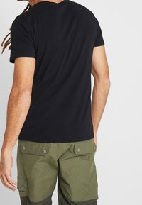 Camiseta de algodón negra de manga corta, combinada con pantalones cargo verde oliva que presentan bolsillos con tapa y detalles de broche de metal.
