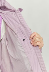 Light purple jacket made of smooth, water-resistant fabric. Features a side pocket and stitched detailing along the opening.