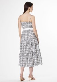 Vestido maxi con estampado floral blanco, con tirantes finos, cuerpo fruncido, falda en capas y una cinturilla blanca. Llevado con sandalias de tacón beige.