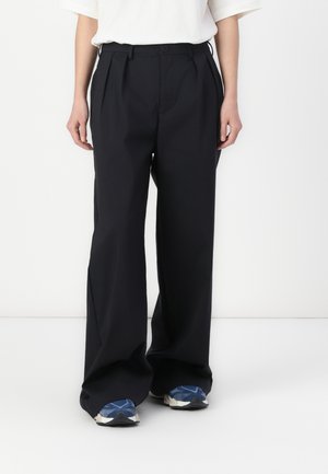 Zwarte wijde broek met hoge taille, voorplooien en knoopsluiting. Draag het met atletiekschoenen met blauwe accenten.